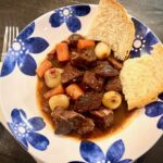 Beef Bourguignon with crusty bread in a shallow blue and white bowl