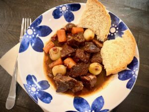 Beef Bourguignon with crusty bread in a shallow blue and white bowl